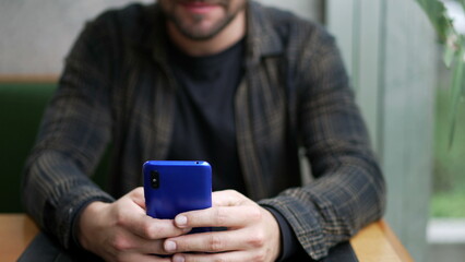 Young man using smartphone sitting at cafe restaurant by window. Person typing message on smartphone closeup hand and face