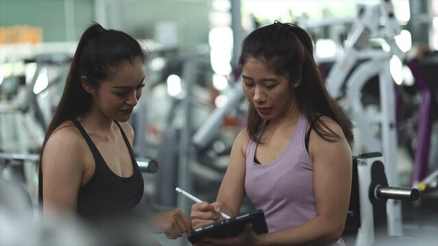 Two women training in a fitness center, a female trainer and a client chatting in the gym to explain the training program details, how to get fit and lose weight. Fitness training concept.
