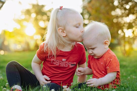 little sisters together in park. Caucasian blonde girl giving flower to her adorable baby sister.
