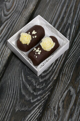 Cake potato. Decorated with butter cream. In a gift box. Against the background of black pine boards. Shot close-up.