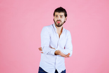 Young man with crossed arms posing against a pink background, casual style with white shirt and dark pants, modern portrait with a vibrant and clean aesthetic