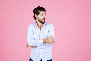 Woman standing against a pink background with crossed arms, wearing a white shirt and dark pants, exuding confidence and casual style