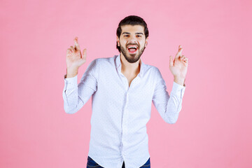 A young man in a white shirt standing against a pink background with hands raised in a gesture of excitement or celebration