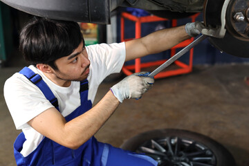 Man technician car mechanic in uniform checking or maintenance a lifted car service at repair garage station. Worker holding wrench and fixing brake discs. Concept of car center repair service.