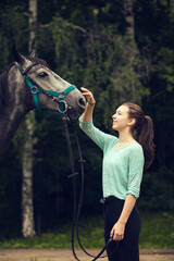 Obraz premium Young girl with grey horse looking at each other. Girl strokes the horse head. Love, care, friendship