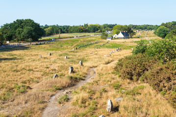 Aerial horizontal view of the mysterious rows of megalithes (menhir) in the archeological site of Carnac, Brittany, France, with a traditional cottage. Blue sky on the background.