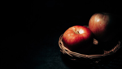 two fresh red apples in a basket On a black background with water droplets, lights are falling with...