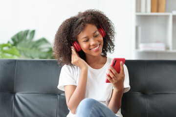 Bright and cute Asian young woman wearing headphones sit on the sofa and using smartphone to listen to music happy and relax listening to music at home.