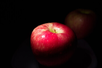 Fototapeta na wymiar fresh red apple On a black background with water droplets, lights are falling with space for text.