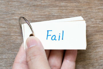 Hand hold flash card with handwriting in word fail on wood background
