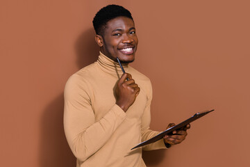 Portrait of attractive trendy cheerful guy filling application form writing test isolated over brown color background © deagreez