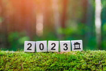 Property 2023 concept. Wooden cubes with numbers 2023 and house icon on mossy fallen tree in summer...