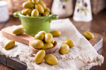 Large green olives in a cup on a wooden table. Italian olives, Sardenya and Greece harvest, olive leaves in the frame. close-up