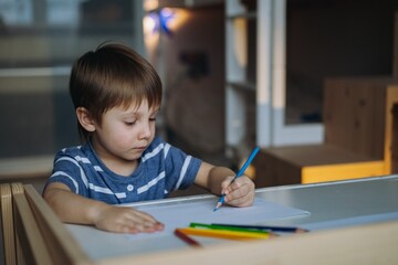 Adorable little toddler boy passionately drawing with color pencils. Image with selective focus