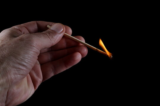 Match stick ignited burning bright fire flame in hand isolated on black