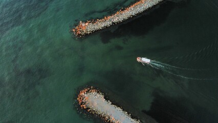 Aerial shot of two rocky piers in the middle of a sea and a boat passing by