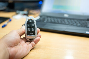 A car digital keyless in the people hand with office working desk as blurred background. Preparing for go back home after finish worked concept scene. Selective focus at the object.
