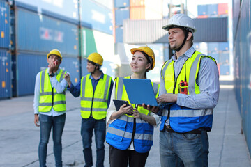 Group of multiethnic technician engineer and businessman in protective uniform standing and discussing, researching, brainstorming and planning work together with computer at container cargo site