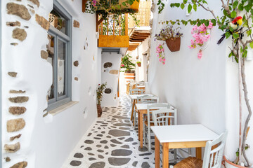Fototapeta na wymiar Naxos island, Cyclades Greece. Traditional outdoors cafe wooden chair table on paved street plants.
