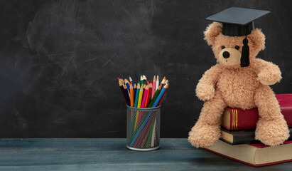 Back to school. Teddy bear with graduation cap books and pencils on desk