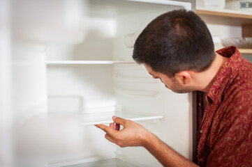 The young man is cleaning the fridge, he has moved into his new apartment