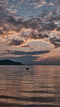 Colorful summer sunset on bay. Scenic dramatic clouds on sky. Boat with two people