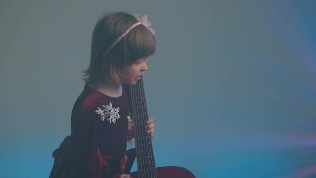 Cute little girl stands on stage in vintage dress and plays an acoustic guitar like a counter bass or cello. The concept of performing the author jazz and blues music. Hobbies and art among children