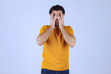 Man in yellow shirt looking through his fingers