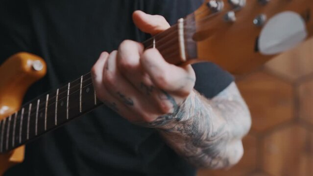 Close up classical wooden guitar in hands of musician with tattoos performing popular composition or new song in style of country demonstrates correct playing of musical instrument sits indoors