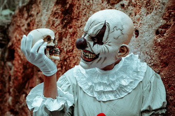 creepy evil clown looking at a skull in his hand