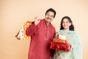 Happy mature indian couple wearing traditional cloths holding shopping bags and gift boxes,...