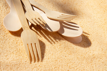 Wooden bamboo cutlery spoons and forks on on natural light yellow background