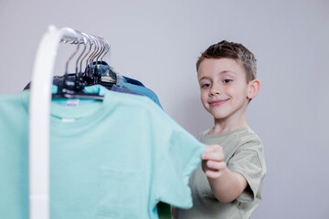 Boy preschooler standing by the hangers, racks up clothes, and chooses clothes for today