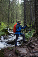 Happy hiker with trekking poles standing in beautiful mountain forest near river. Enjoy his adventure. Activity and sport concept. Healthy hobby