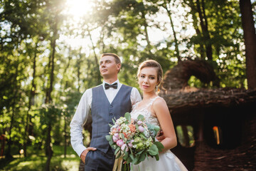 Stylish groom in a suit and a cute brunette bride in a white dress in the forest