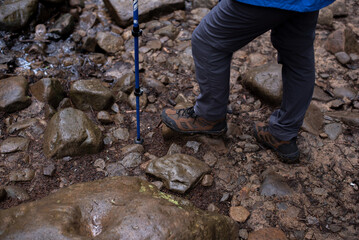 Close up of legs of  man with trekking boots  and poles on the trail. Rocks and stones in mountain forest. Sport and activity concept.  Background with professional hiking shoes and sticks.