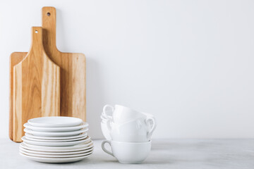 Stack of white porcelain plates and cups with wooden cutting boards on gray stone background