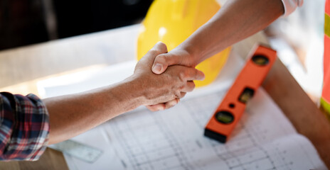 Contructor and Customer home buyer handshake for success construction building project contract complete on blueprint drawing yellow helmet on the desk background
