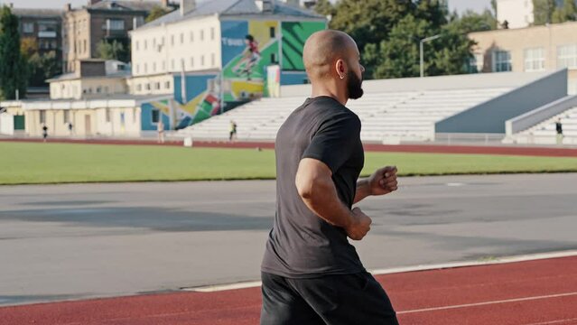 Cropped bald man runs on stadium track in summer morning