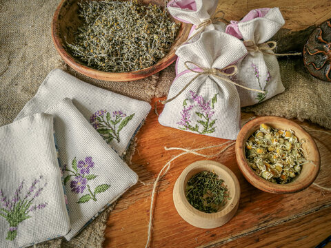 Textile sachet pouches with dried flowers and herbs on wooden table, on sackcloth background.