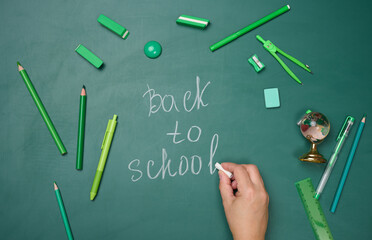School supplies on empty green chalk board, top view.