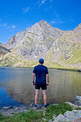 Man looking away celebrates reaching Ibon Azul Superior, a lake in the Aragon region of the Spanish Pyrenees, with Pico Piedrafita behind