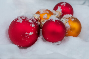 Toys for decorating a Christmas tree in red and gold color lie in the snow. Close up photo