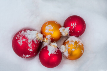 Toys for decorating a Christmas tree in red and gold color lie in the snow. View from above