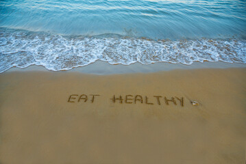 Eat healthy  written in the sand on the beach with the sea washing up the shore