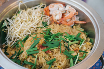 Noodles and shrimp pad thai cooked in a metal bowl.