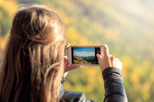 a young woman takes pictures of nature on a smartphone, a view from the back. active lifestyle and impressions