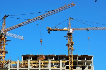View of construction cranes and reinforced concrete houses under construction