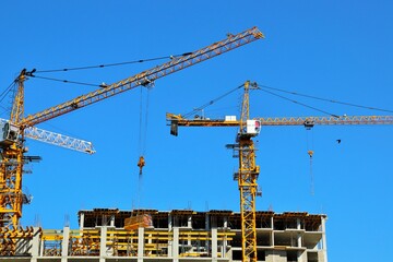 View of construction cranes and reinforced concrete houses under construction