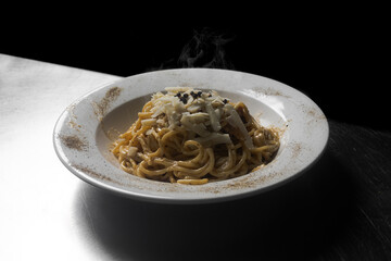 Plato de espaguetis servidos con especies y queso, en plato blanco redondo y fondo negro - obrazy, fototapety, plakaty
